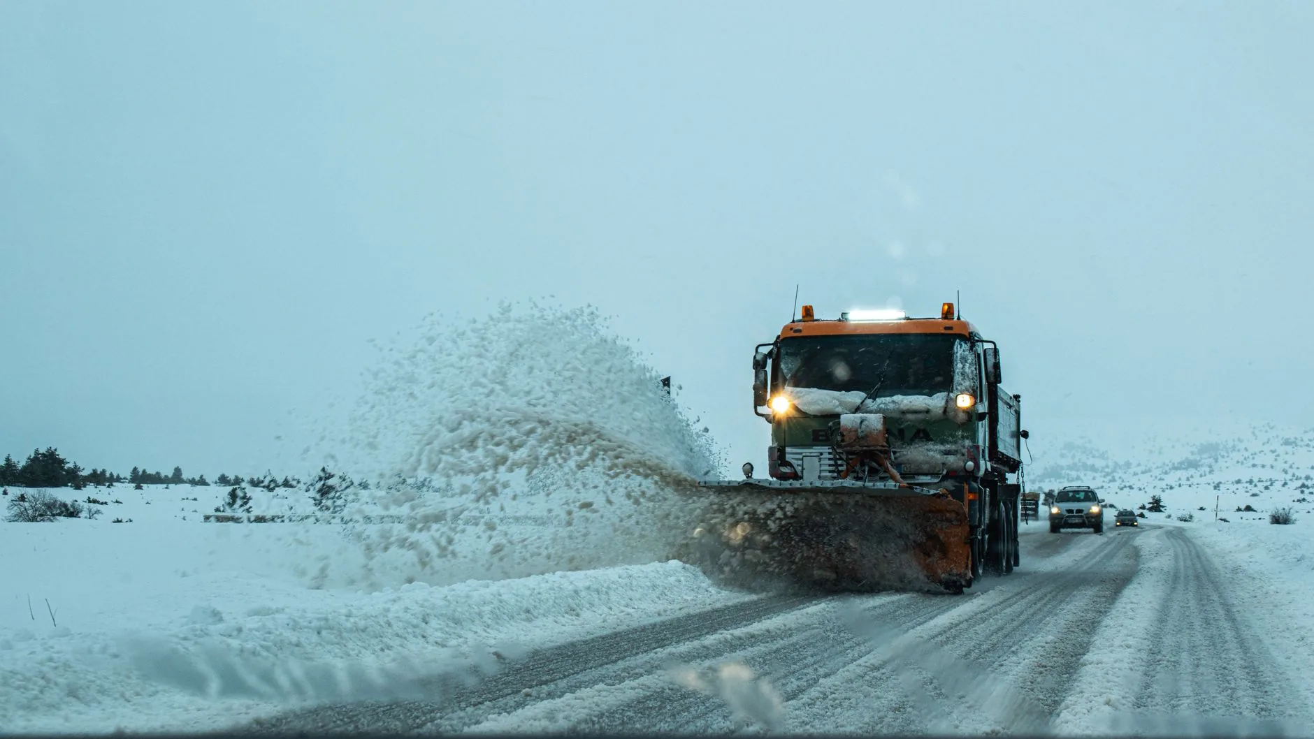 An orange plow truck throwing snow off a winter road