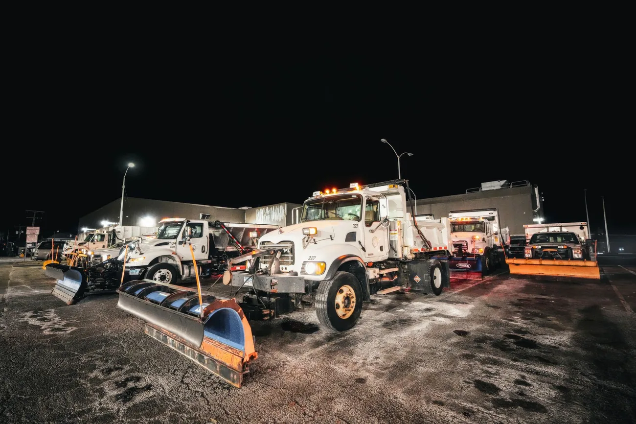 A fleet of plow trucks staged at night