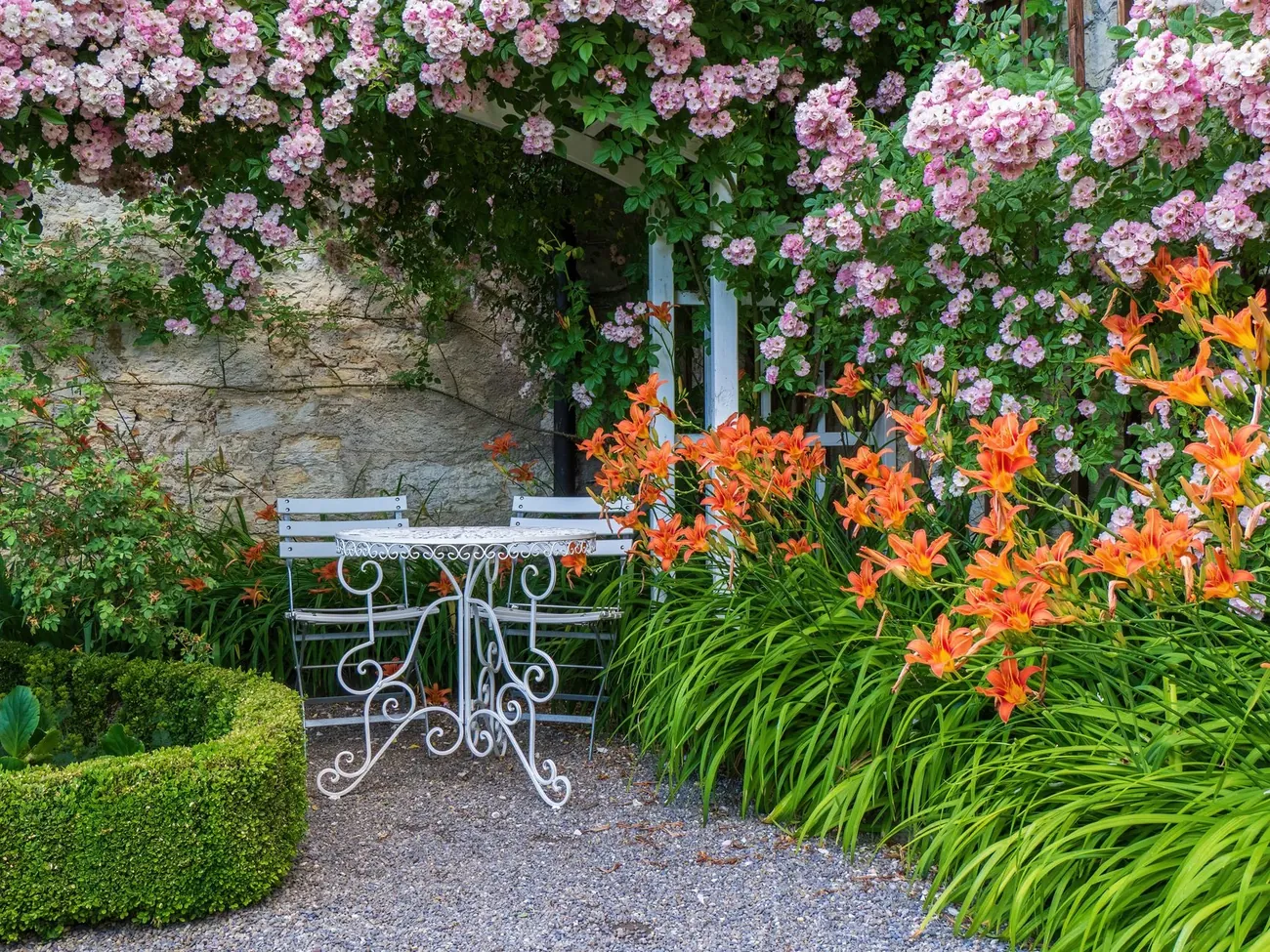 A rose covered arch over a white bistro table in a gravel garden