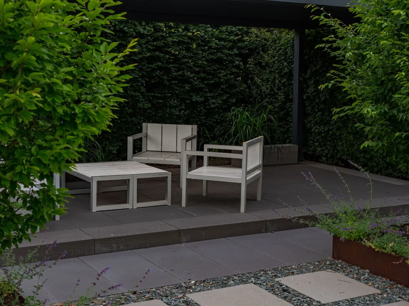 A modern London garden with a covered terrace, white chairs and stepping stones in gravel