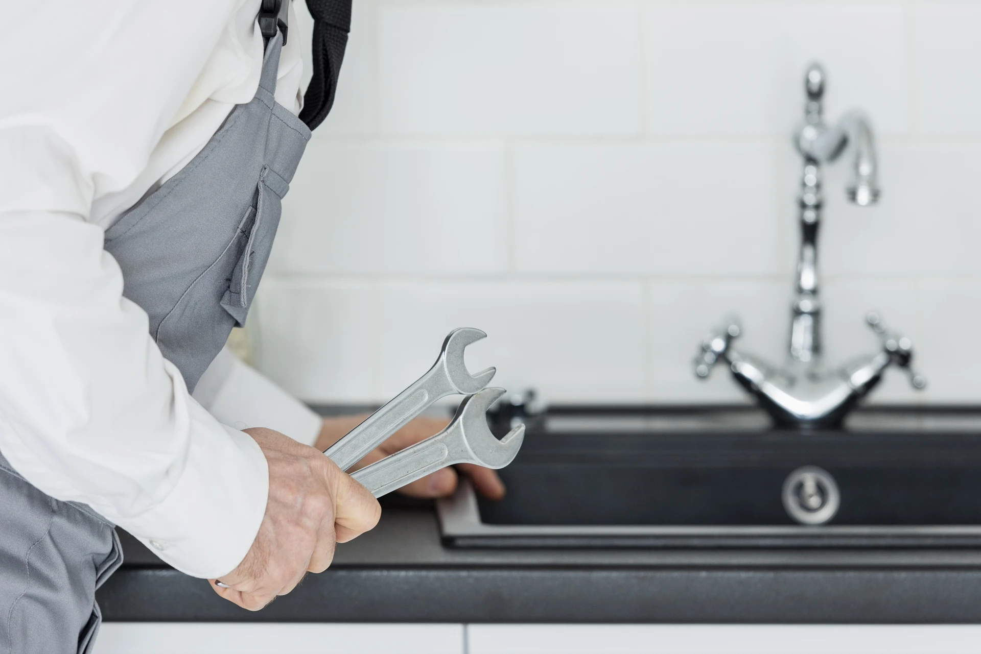 Plumber holding wrenches beside a kitchen sink