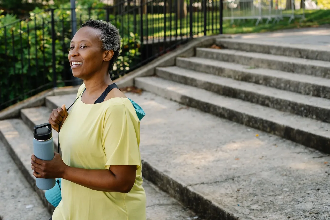 A smiling woman in a yellow top holding a water bottle at the foot of some stone steps