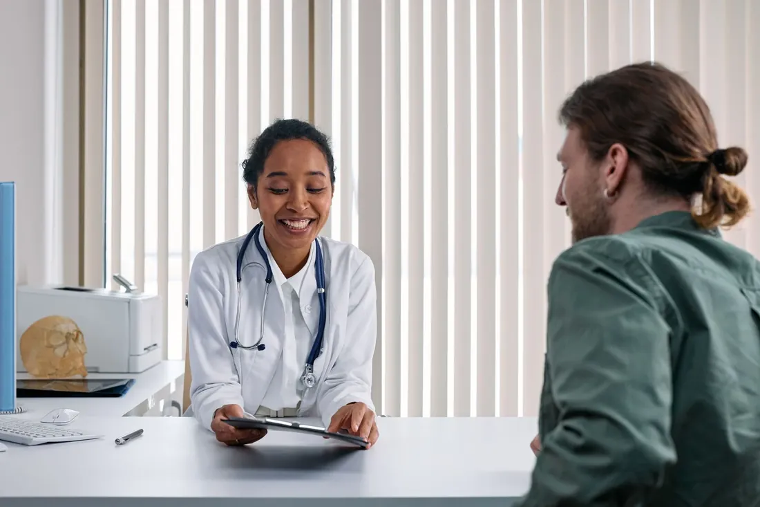 A smiling doctor with a tablet talking with a patient across a desk