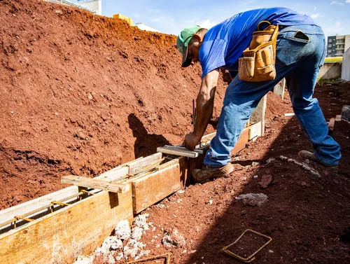 A worker in a trench of red clay beside a foundation form