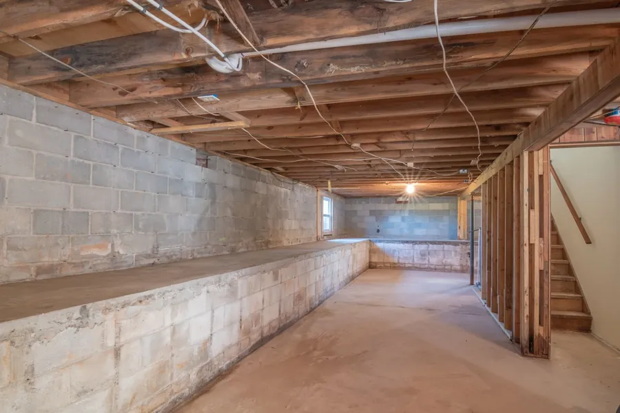 An unfinished basement with bare block walls and exposed joists