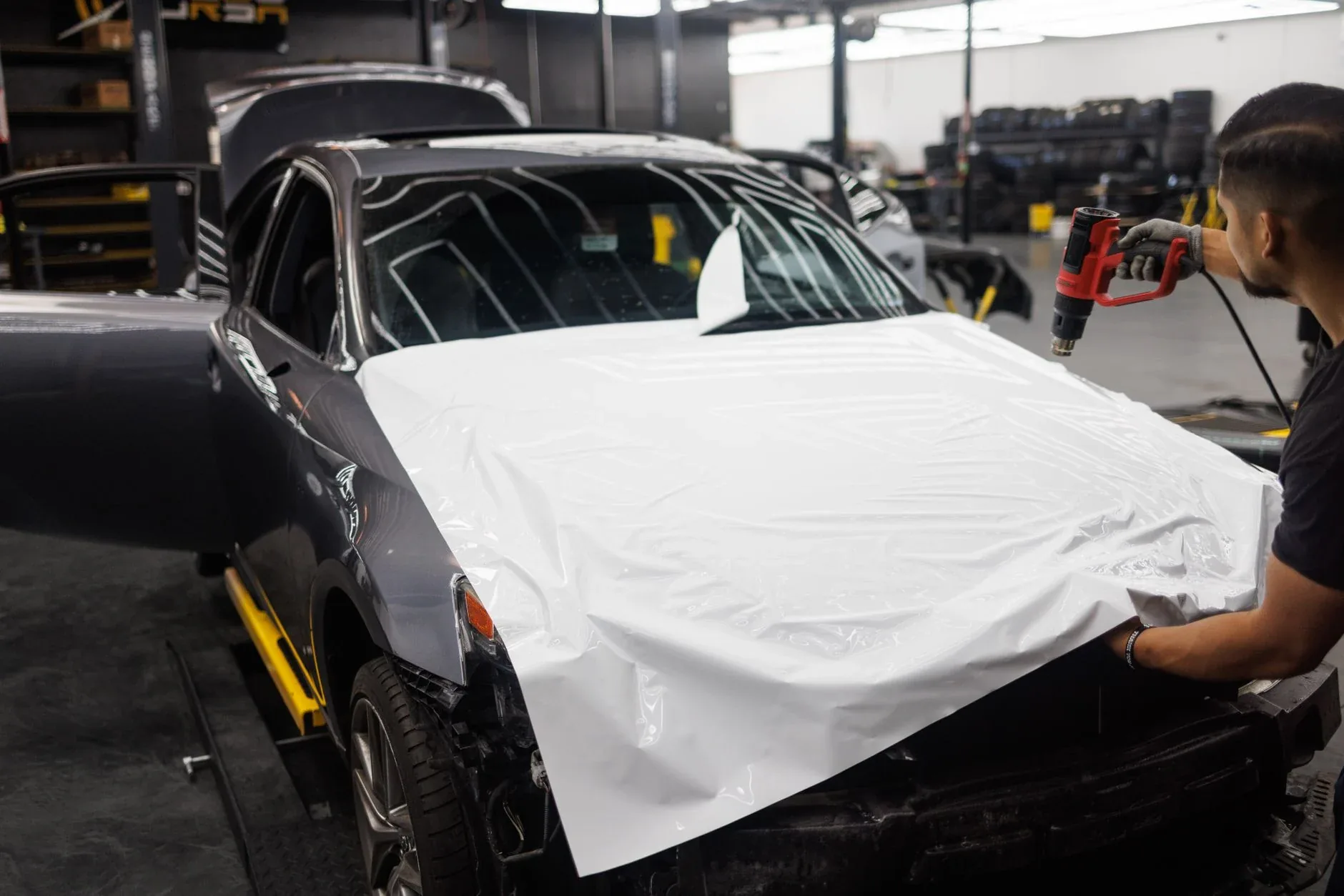 Two installers laying protective film across a bonnet in a bright studio