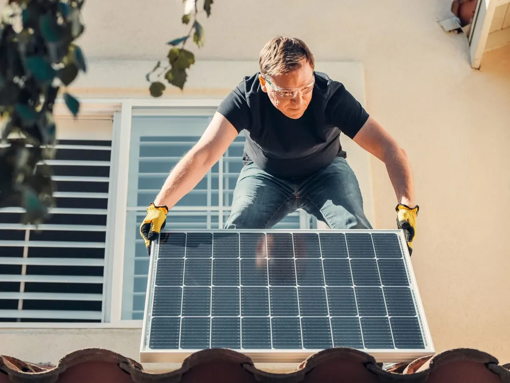 An installer lifting a solar panel onto a tile roof