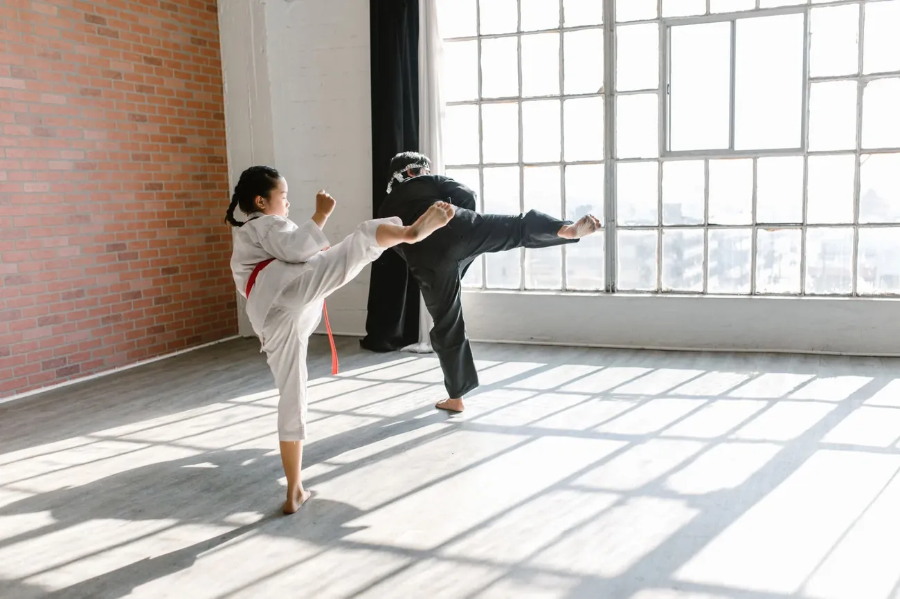 A young student throwing a kick beside her instructor in a sunlit studio