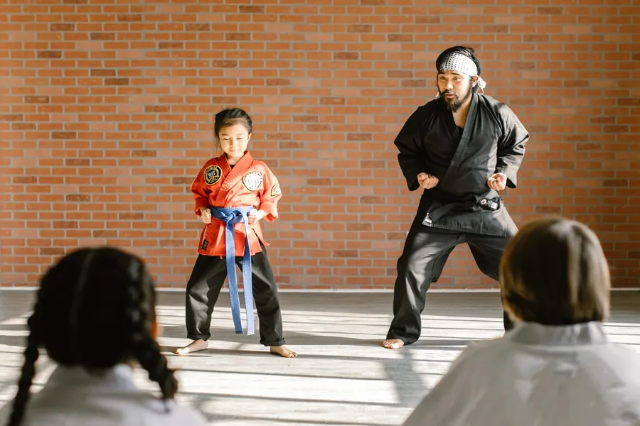 An instructor teaching a young student a stance in a brick walled studio