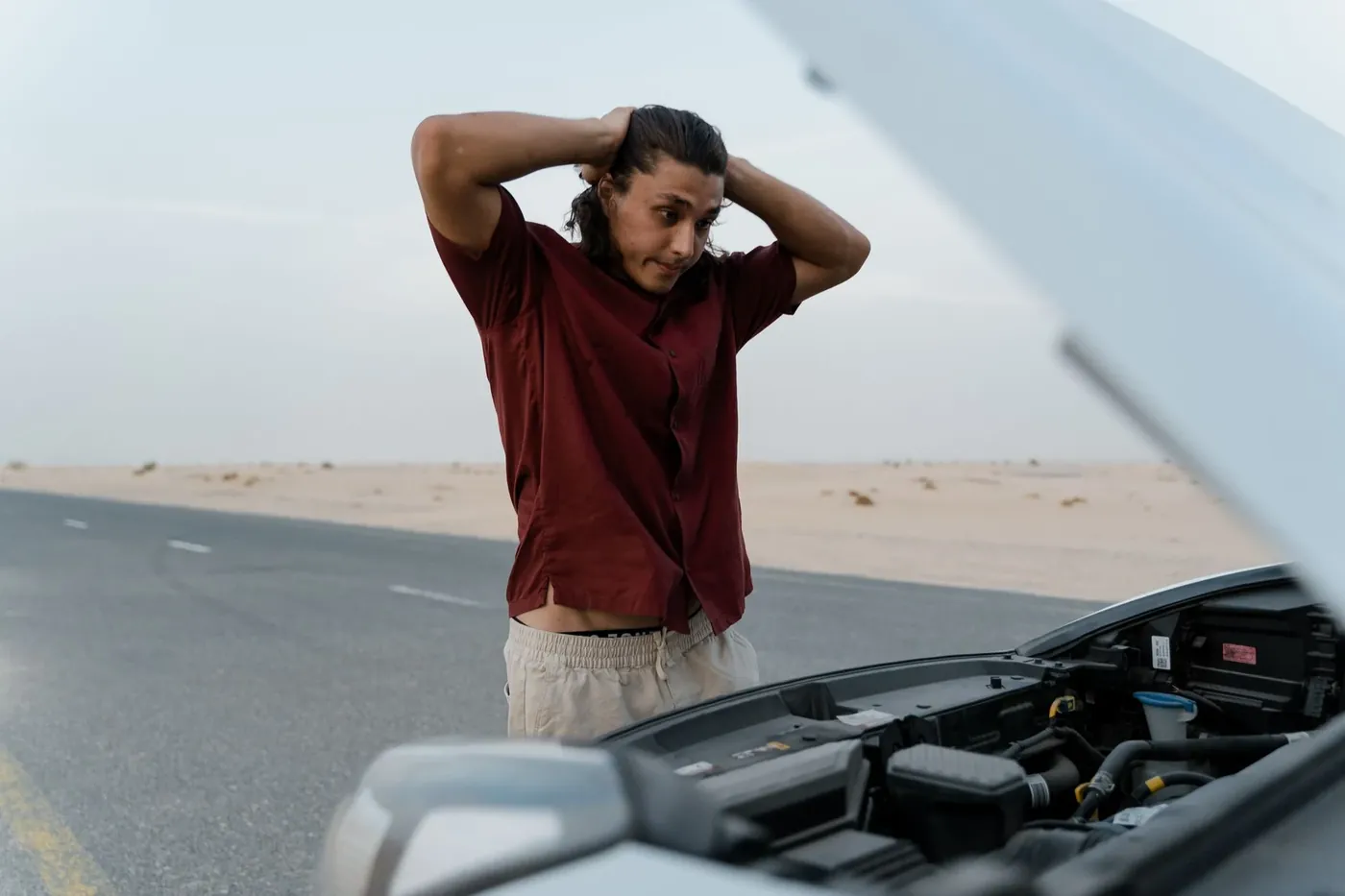 A driver standing beside his broken down car on a highway