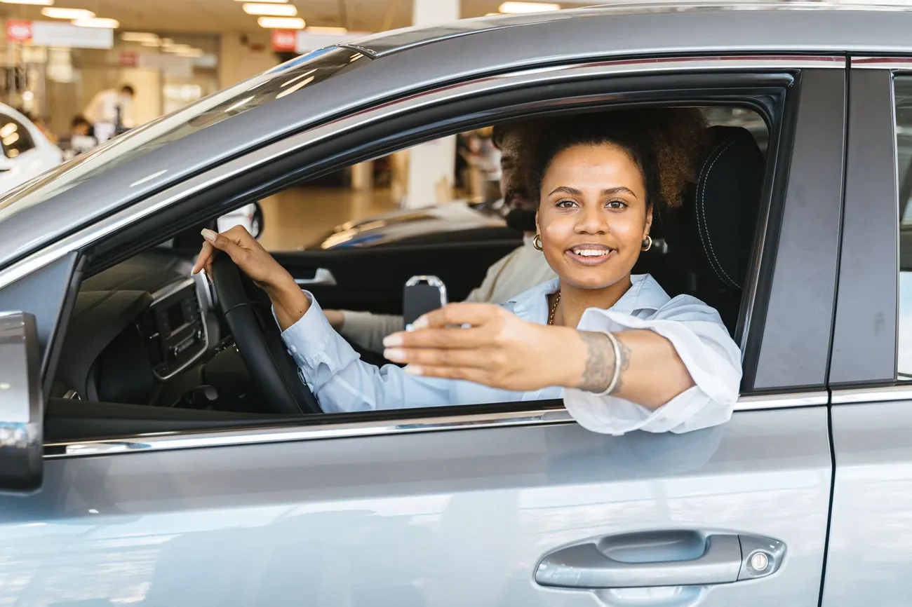 A smiling driver holding the keys through the open window of a silver car