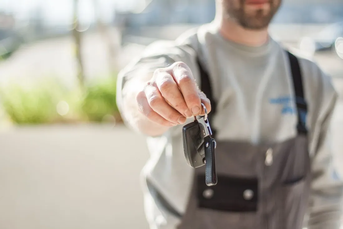 A mechanic in overalls holding out a set of car keys