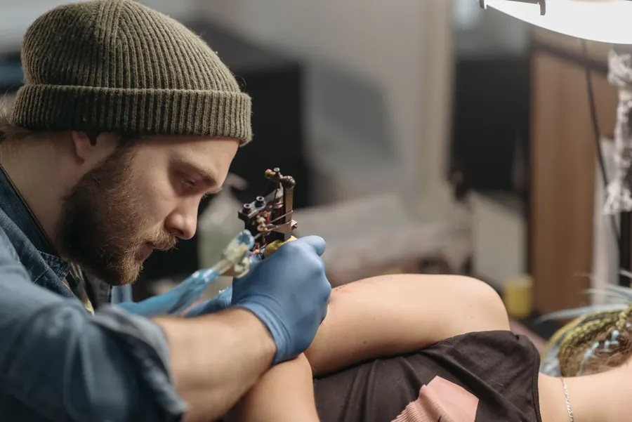 An artist working on a client's arm under a bright lamp