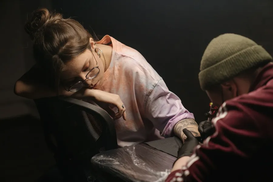A tattoo artist leaning in with a machine while a client rests