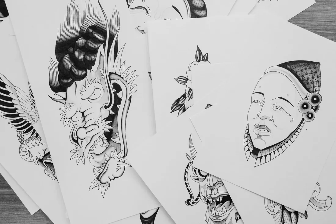 Flash sheets of tattoo designs spread across a table with brushes