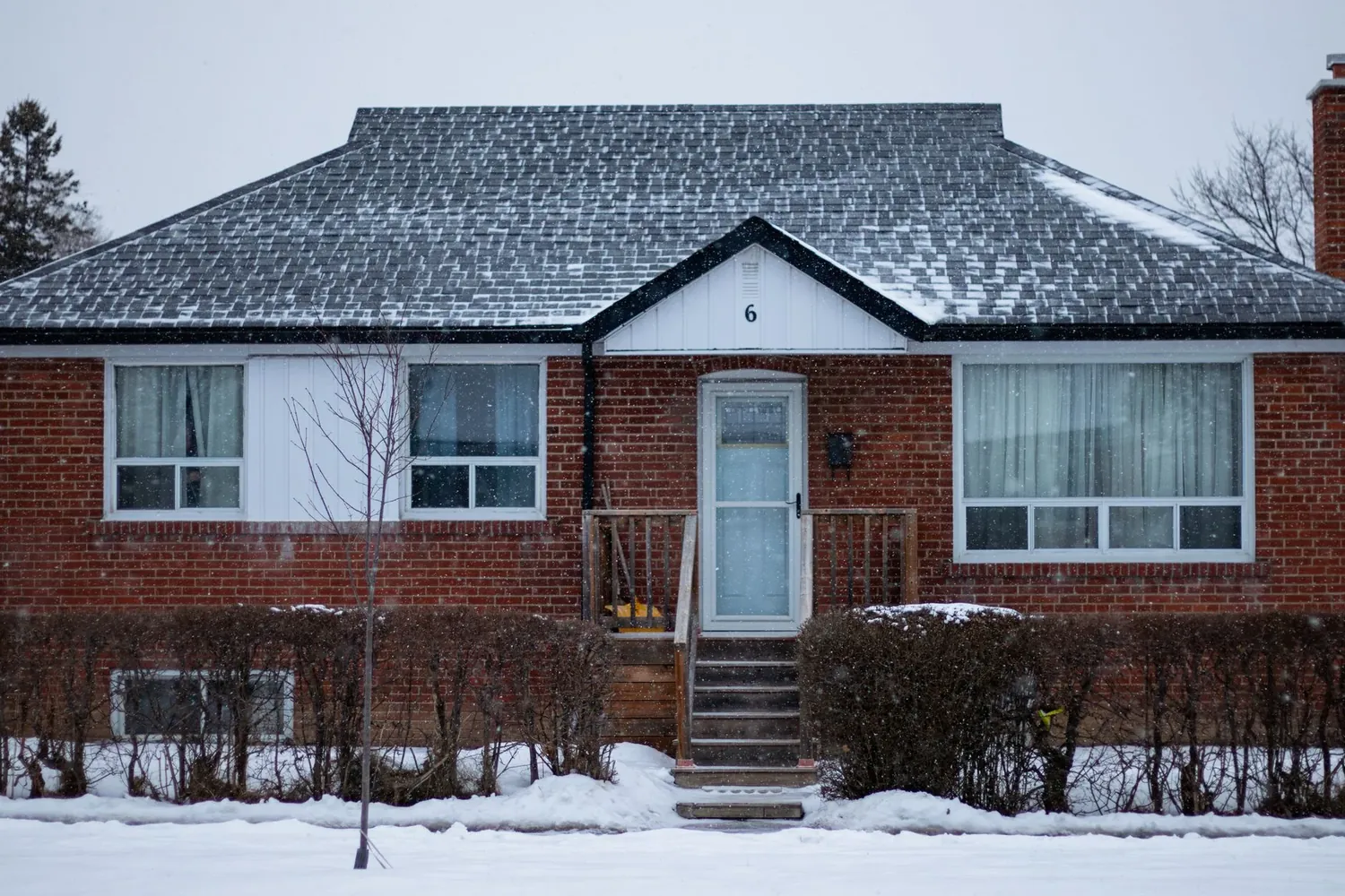 A red brick bungalow in the snow, half shown as a thermal image with its walls glowing orange