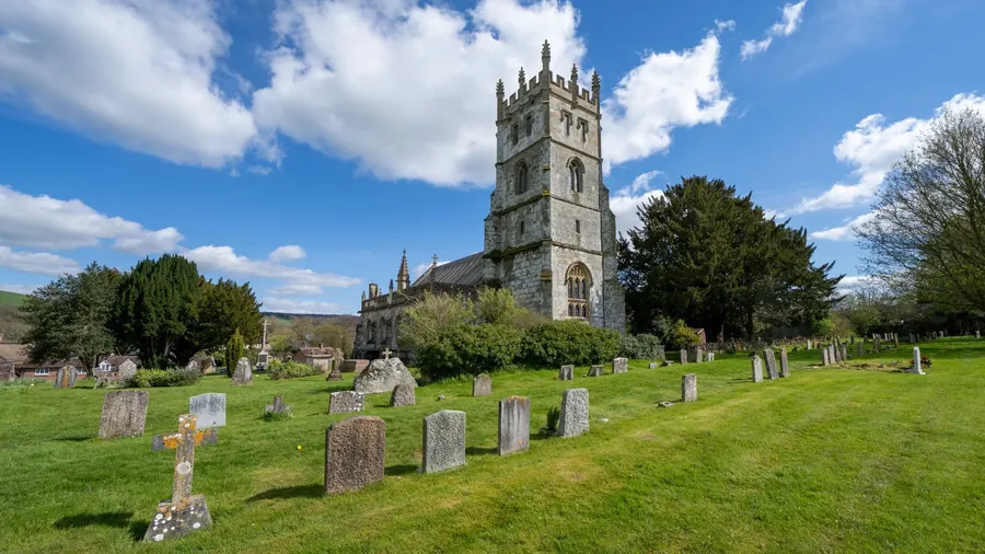 A stone church with a tower and a churchyard under a blue sky